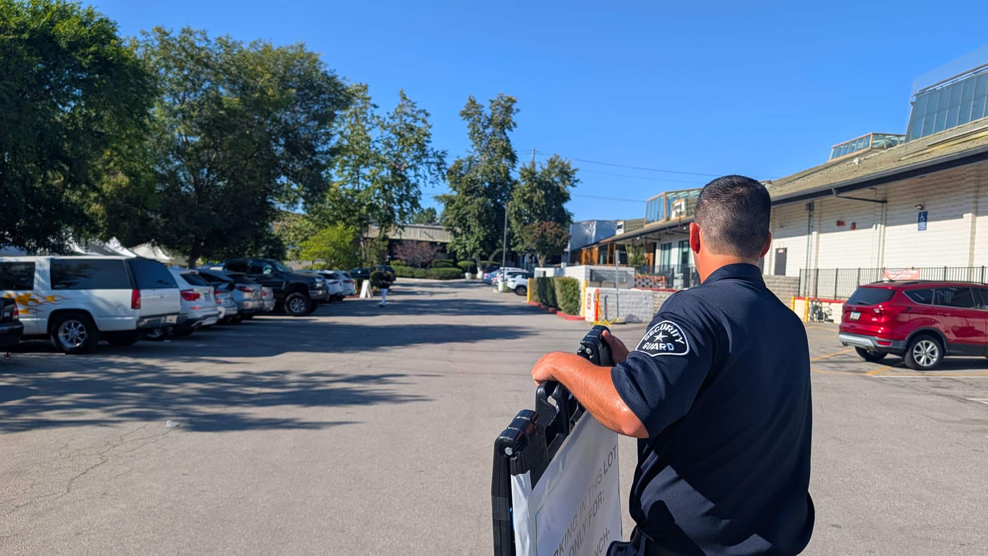 A uniformed security guard on patrol in a commercial property parking lot on a sunny day